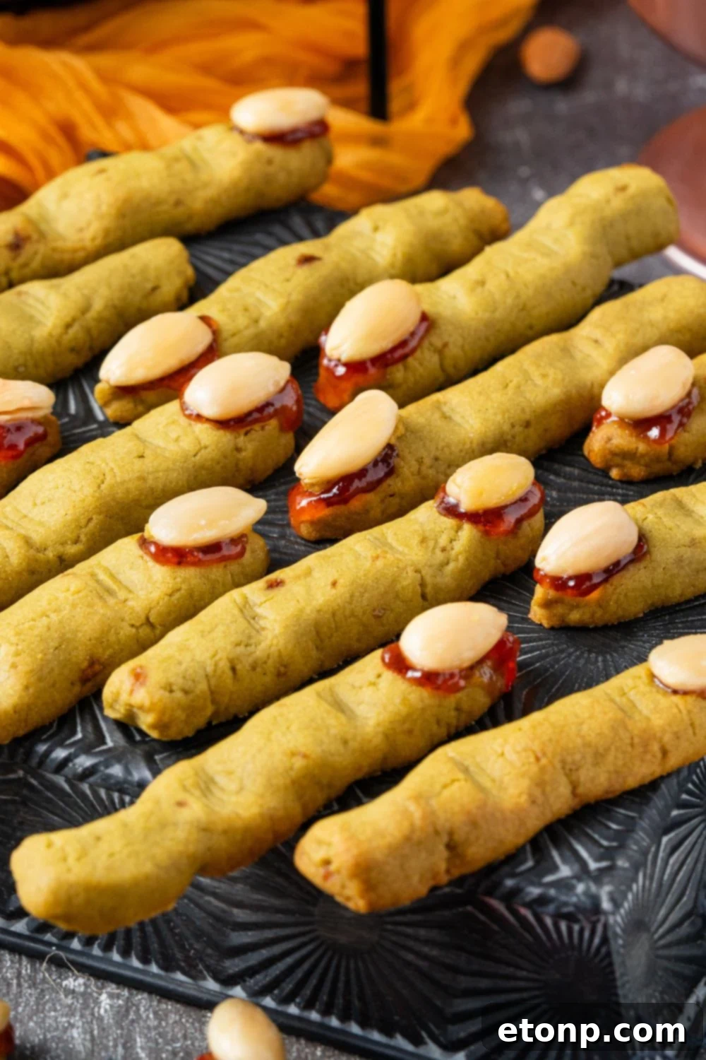 Witch Finger Cookies on a black tray on table with an orange towel behind it on the grey table 