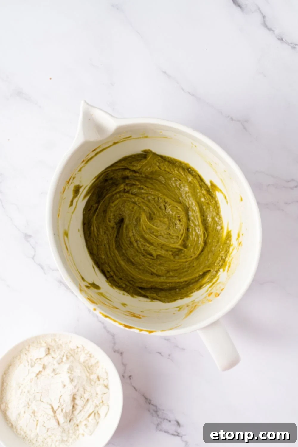 green pistachio cookie dough in a white bowl on table with pistachio butter and vanilla to side 