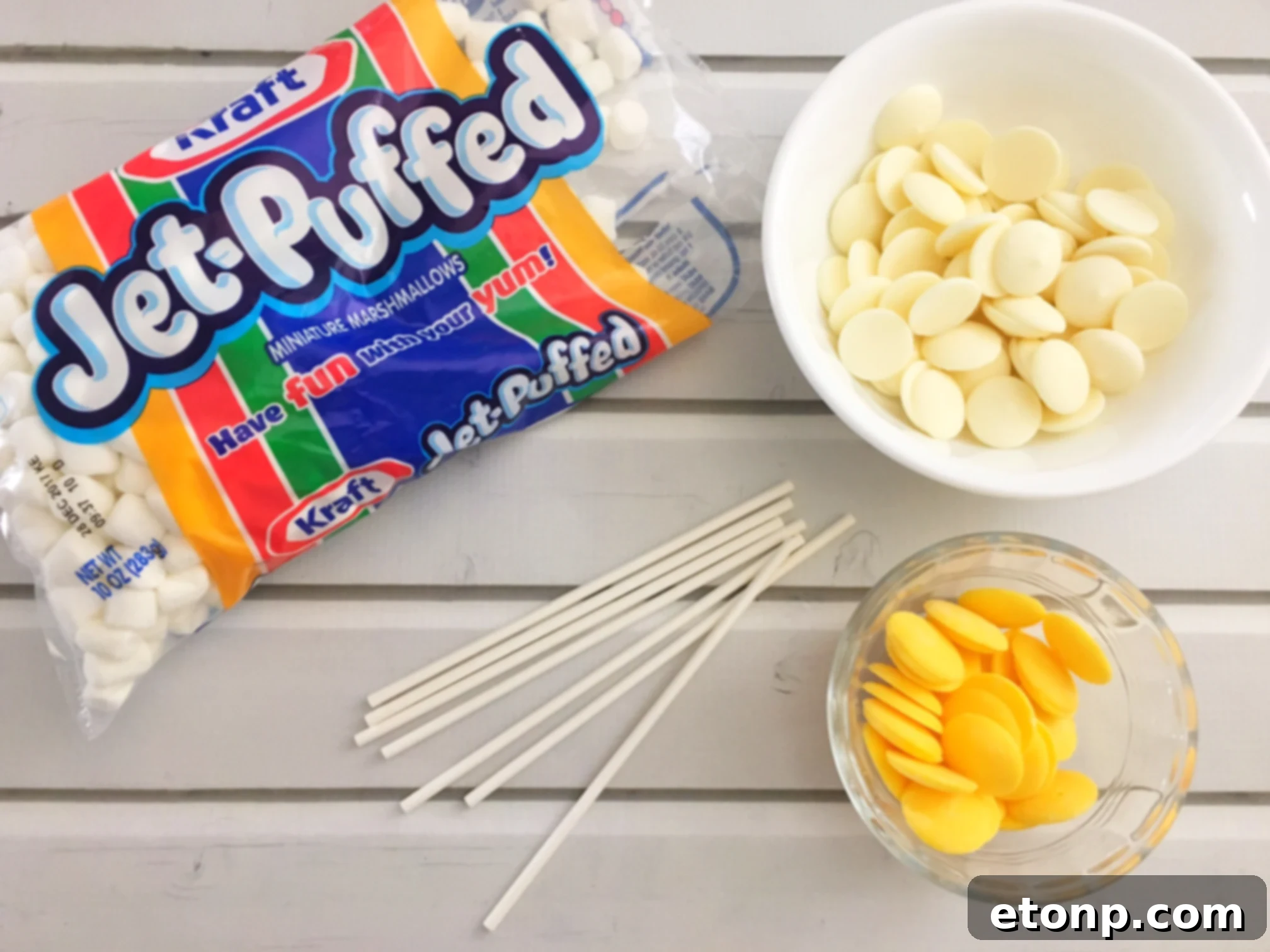Close-up of a 'dirty Q-tip' treat, showcasing the marshmallow ends dipped in white and yellow candy melts on a lollipop stick.