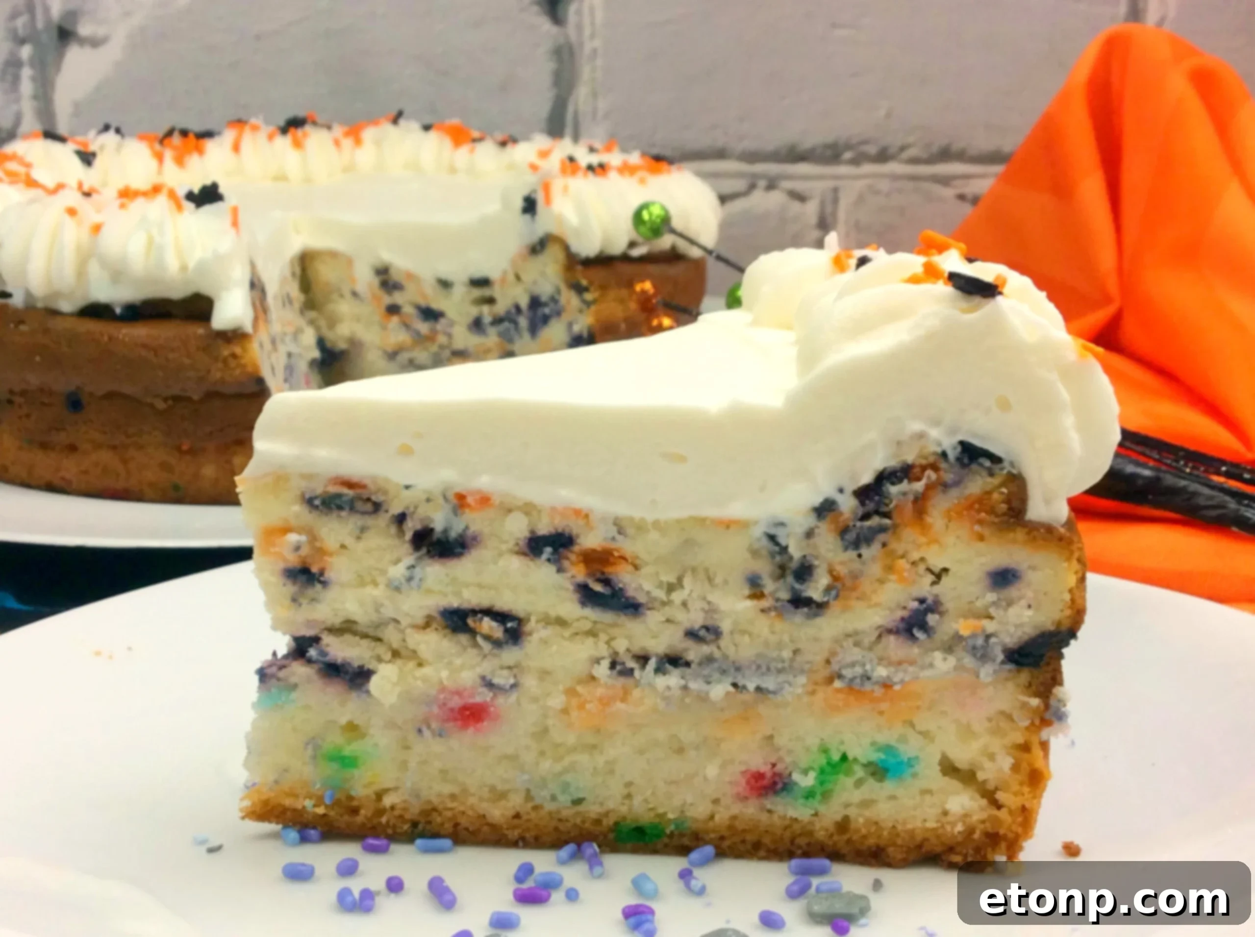 Vibrant Halloween Cheesecake slice showing funfetti cake, creamy cheesecake, and whipped topping with sprinkles