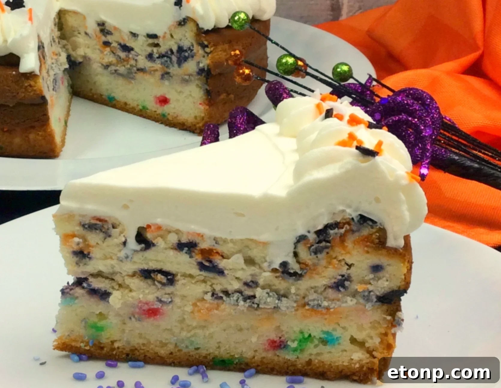 A close-up shot of a slice of Halloween Cheesecake, highlighting the funfetti cake base and the rich cheesecake layer