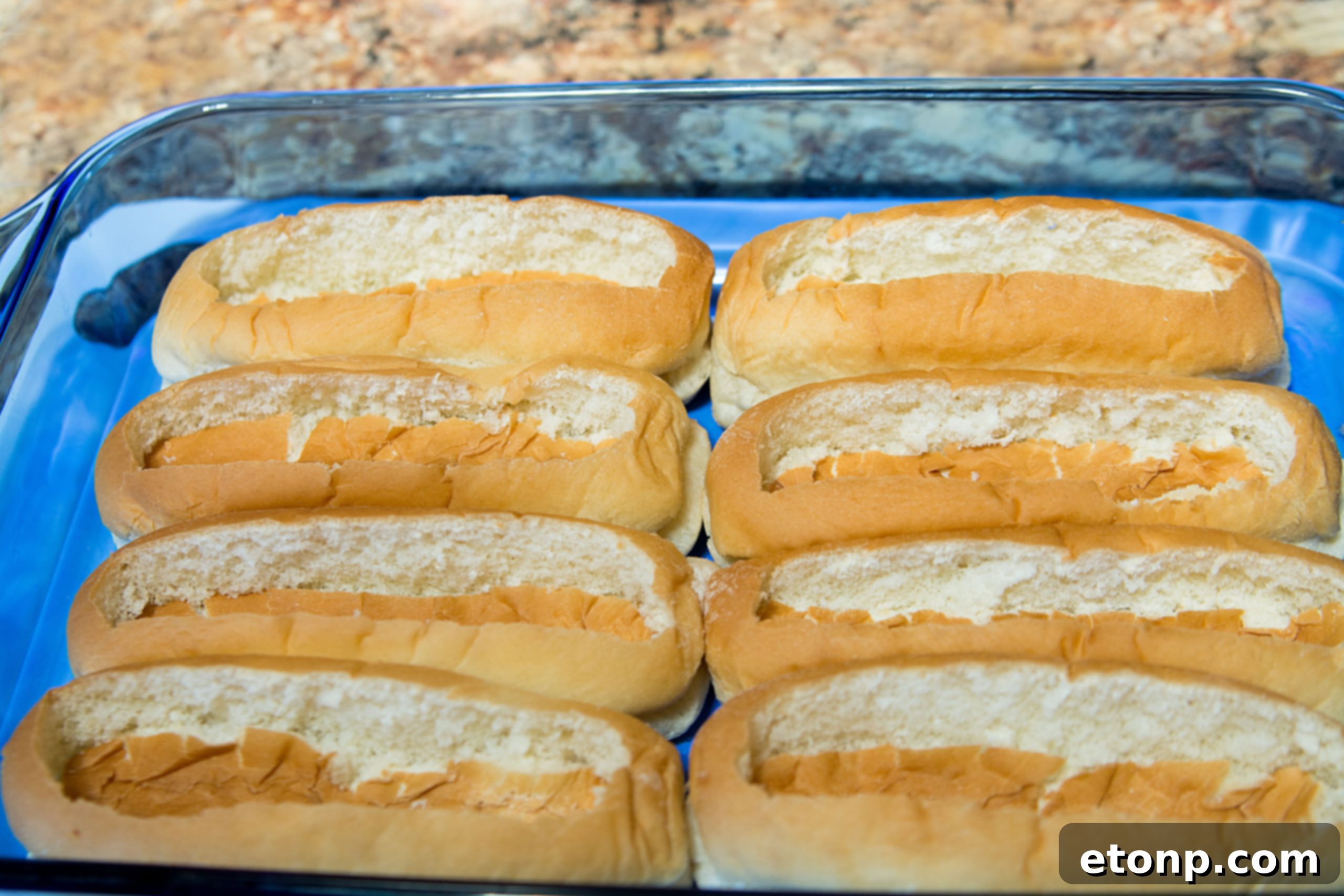 Detailed shot showing how to cut and press down the center of hot dog buns to create a 'boat' shape.