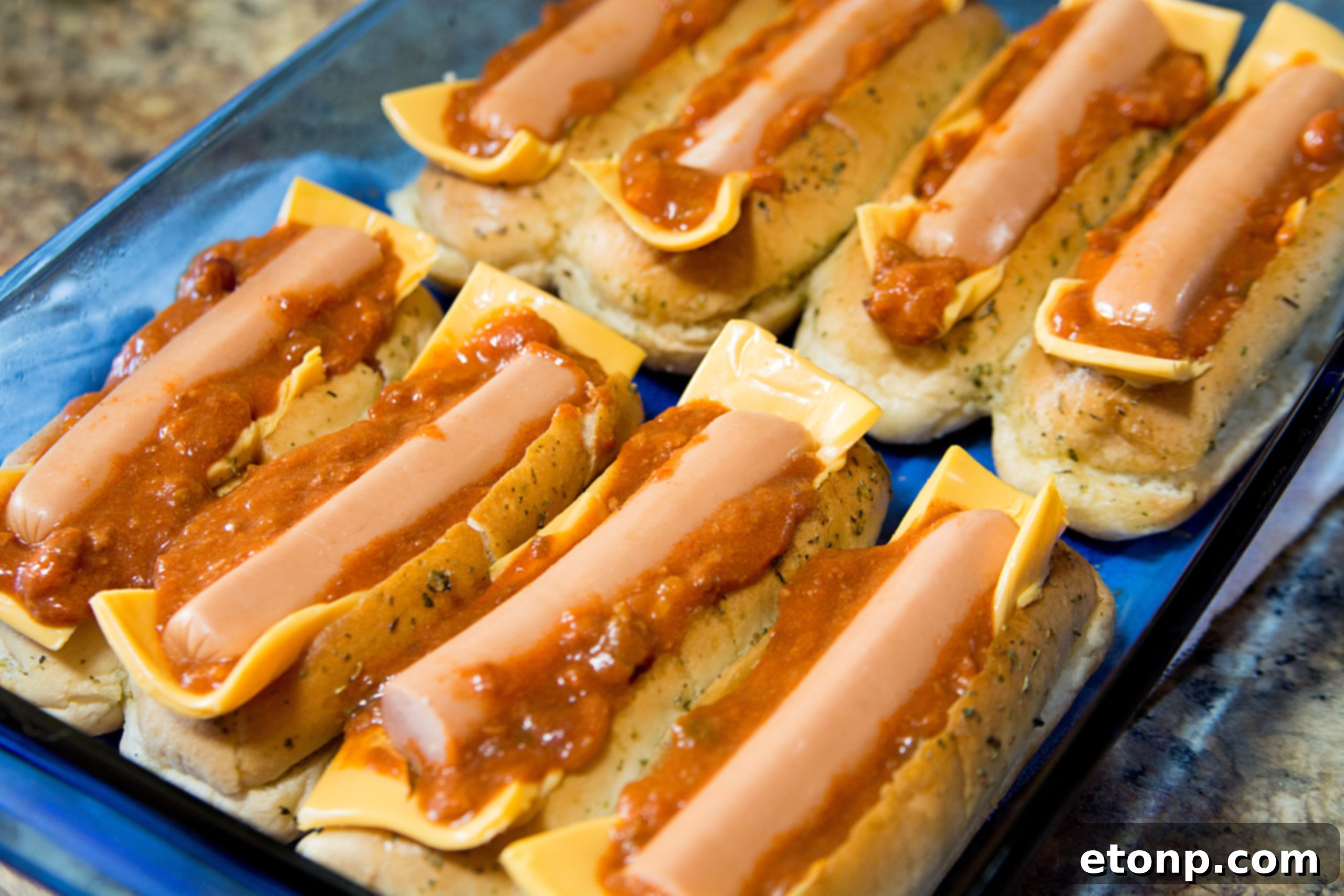 Loaded Chili Cheese Dog Boats 10 Chili cheese dog boats fully assembled with hot dogs and topped with more chili, ready for final baking.