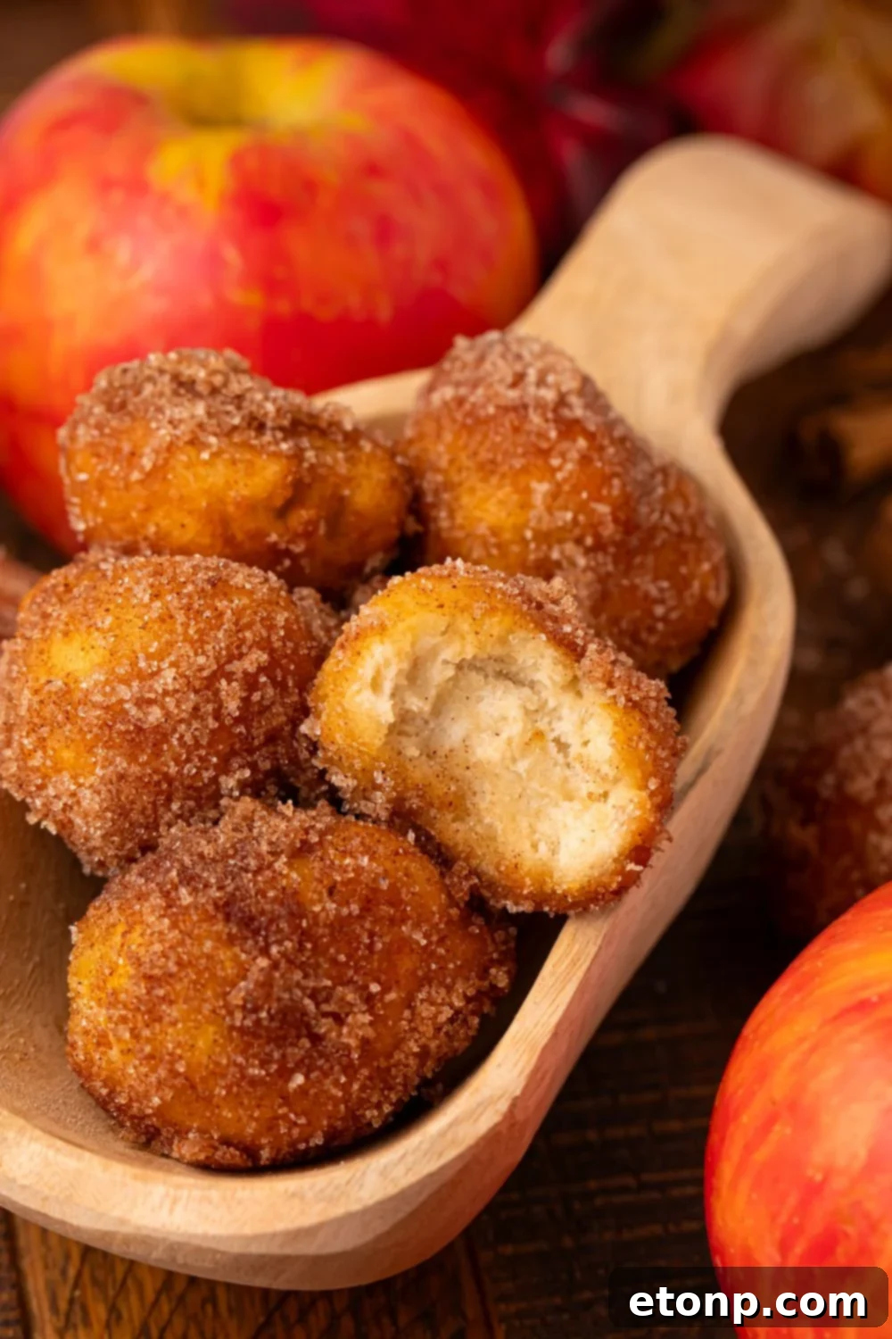 Apple Pie Donut Holes  in a wooden spoon on table with some apples beside the spoon 