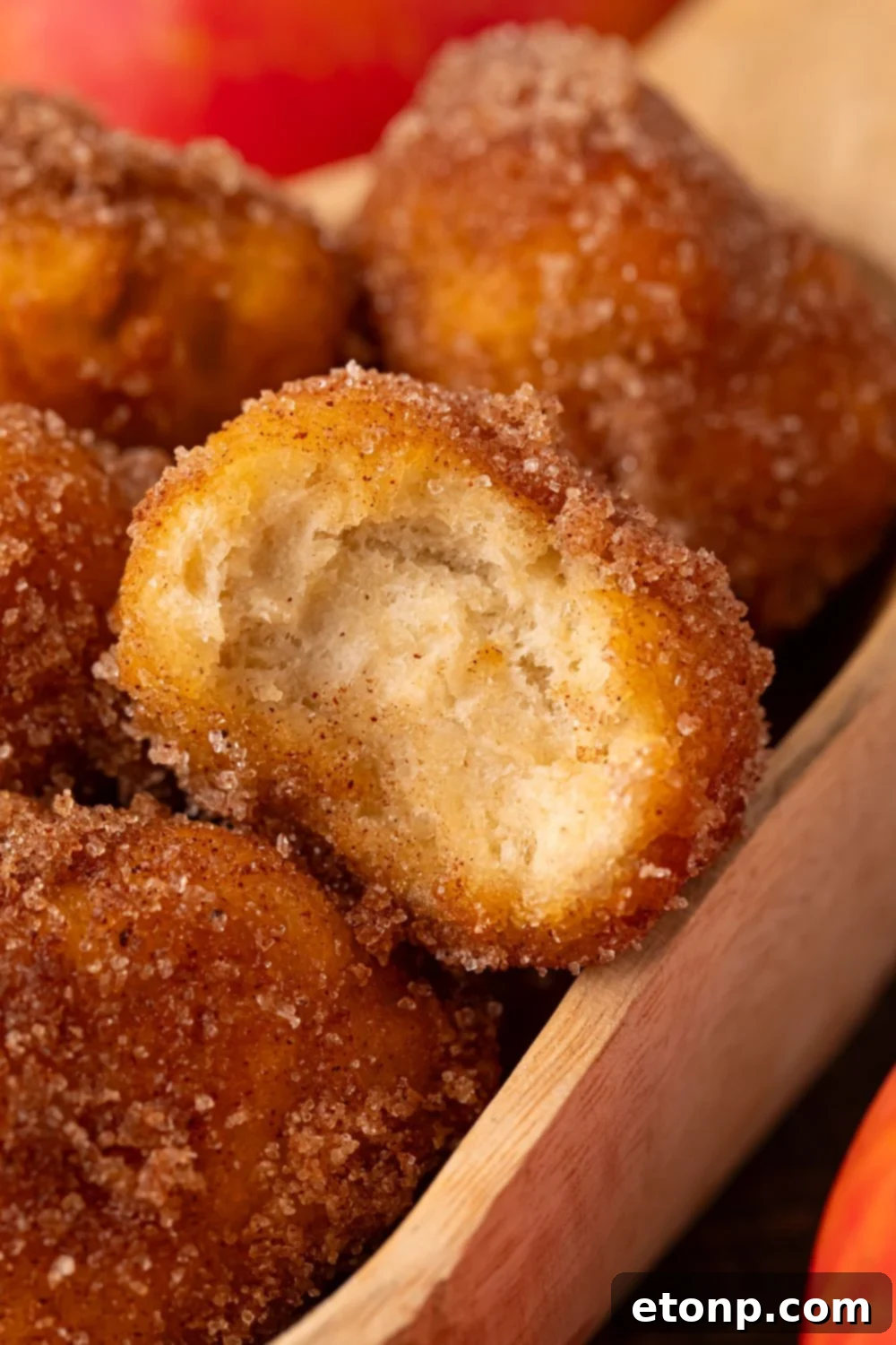 Apple Pie Donut Holes in a wooden spoon with one with a bite taken out of it sitting on top 