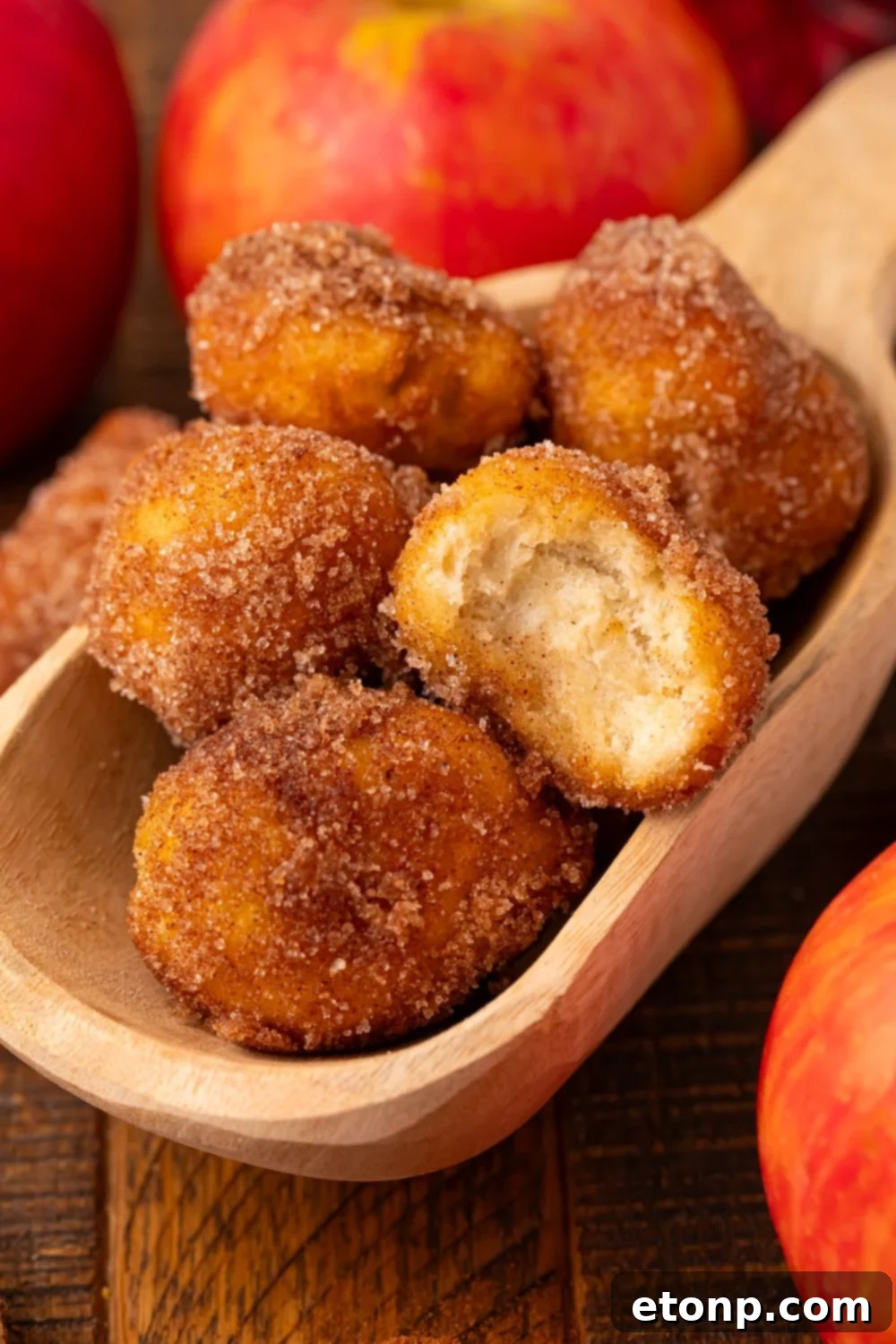 wooden spoon with a handful of Apple Pie Donut Holes sitting on a wooden table with apples around it 