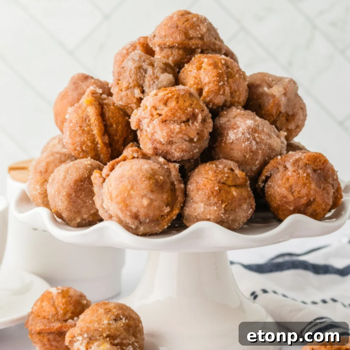 Pumpkin Spice Donut Holes stacked on a cake platter sitting on table with more donut holes scattered around the table 