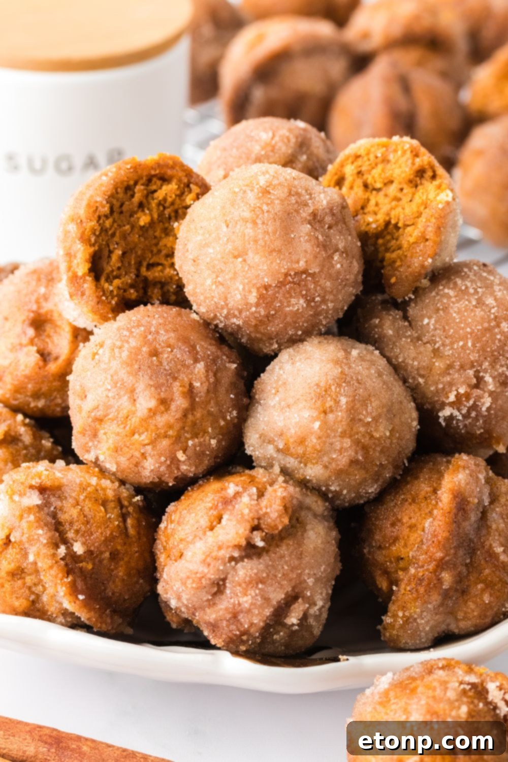 Pumpkin Spice Donut Holes stacked on a plate with a few cut in half to show the centers of the donuts 