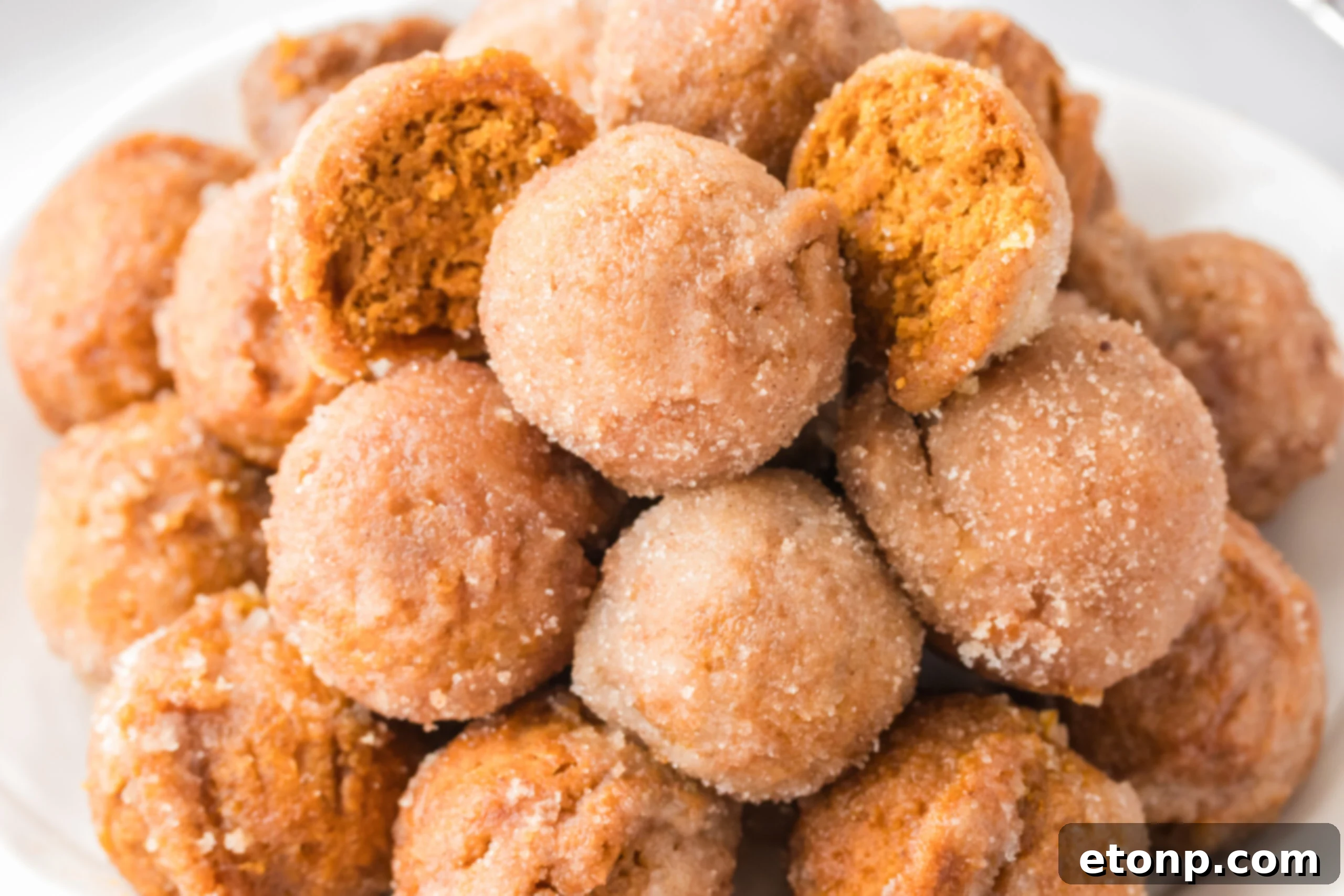 Pile of Pumpkin Spice Donut Holes on a white plate with one cut open to see the inside 