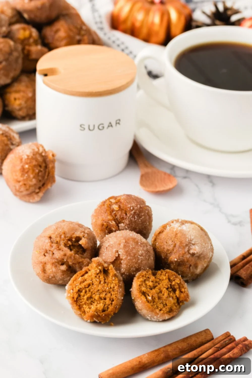 plate with pumpkin spice donut holes and some are cut in half. A cup of coffee, cinnamon sticks andmore around table