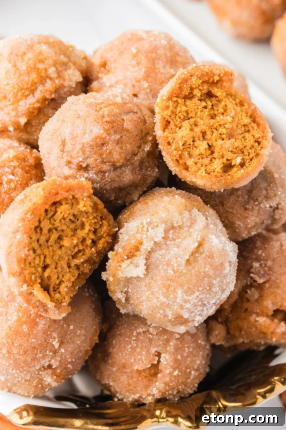 Pumpkin Spice Donut Holes stacked on a platter with one cut in half to see the fluffy center of the donut holes 