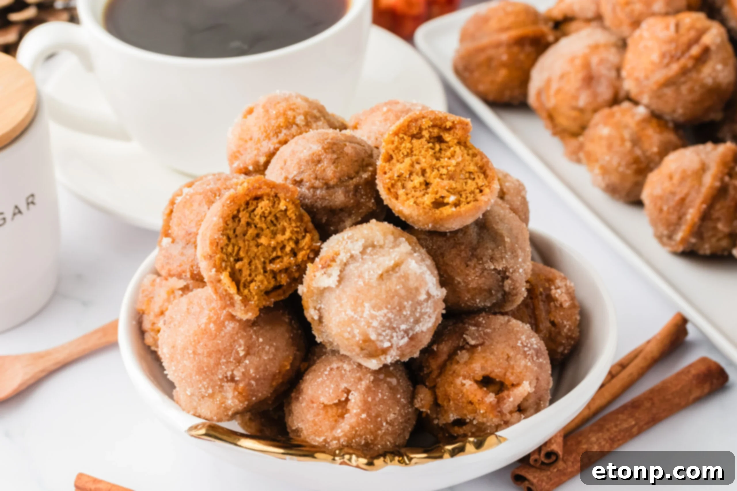 Pumpkin Spice Donut Holes on a white plate with a cup of coffee in the background