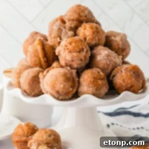 Pumpkin Spice Donut Holes stacked on a cake platter sitting on table with more donut holes scattered around the table
