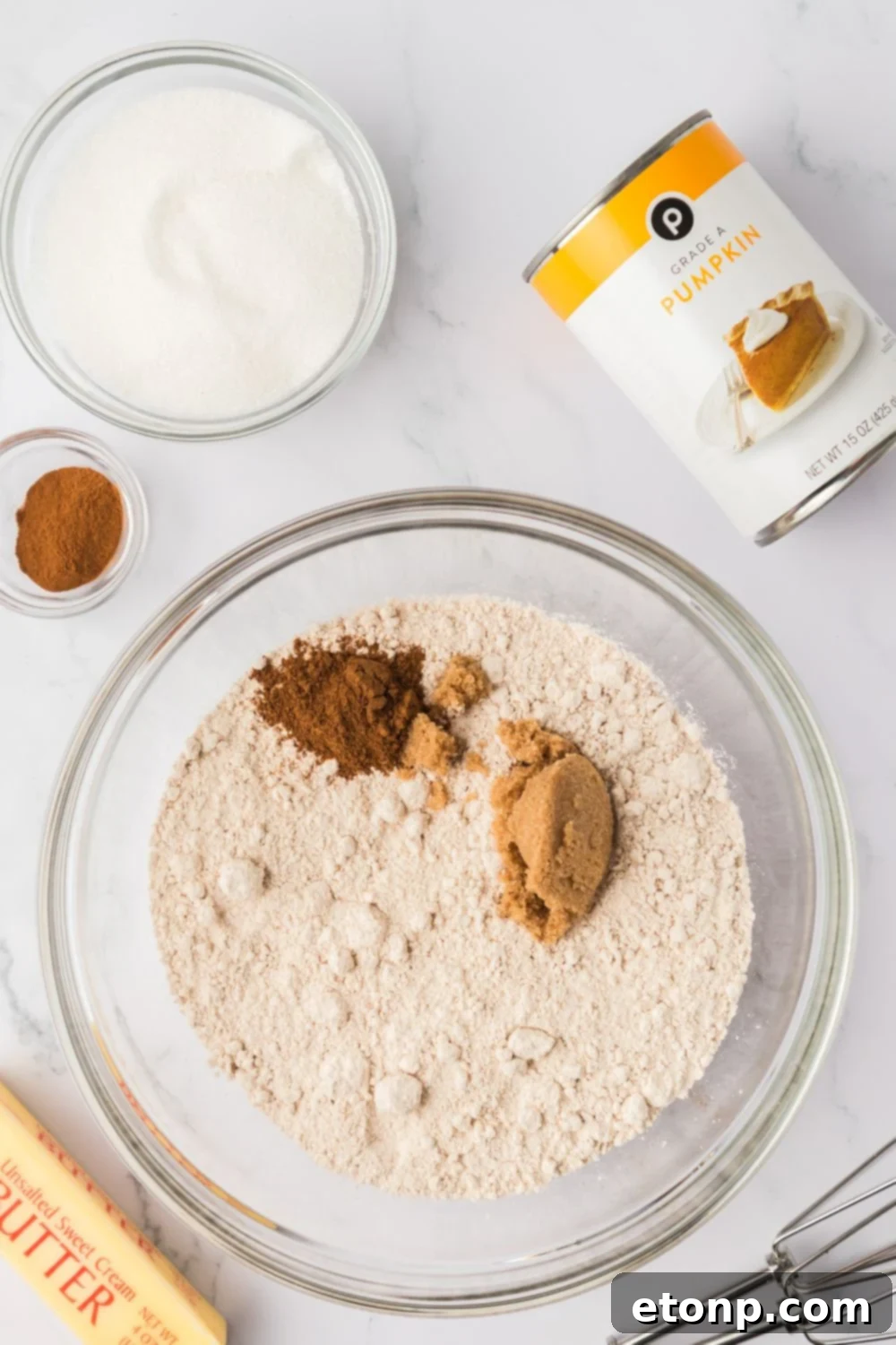dry ingredients for making pumpkin donuts in a glass bowl with a can of pumpkin puree to the side and a stick of butter