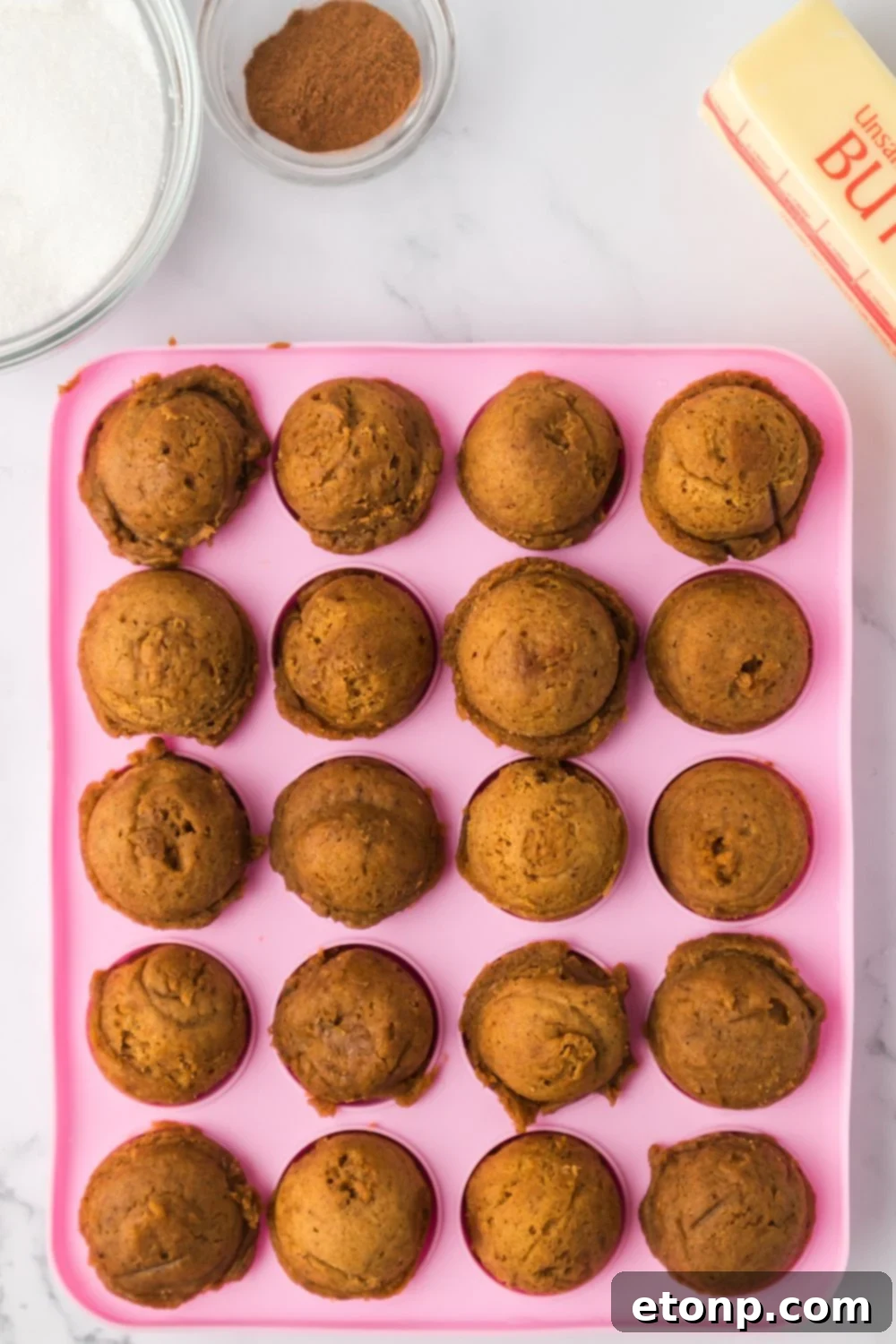 baked Pumpkin Spice Donut Holes in a pink pan sitting on a marble counter