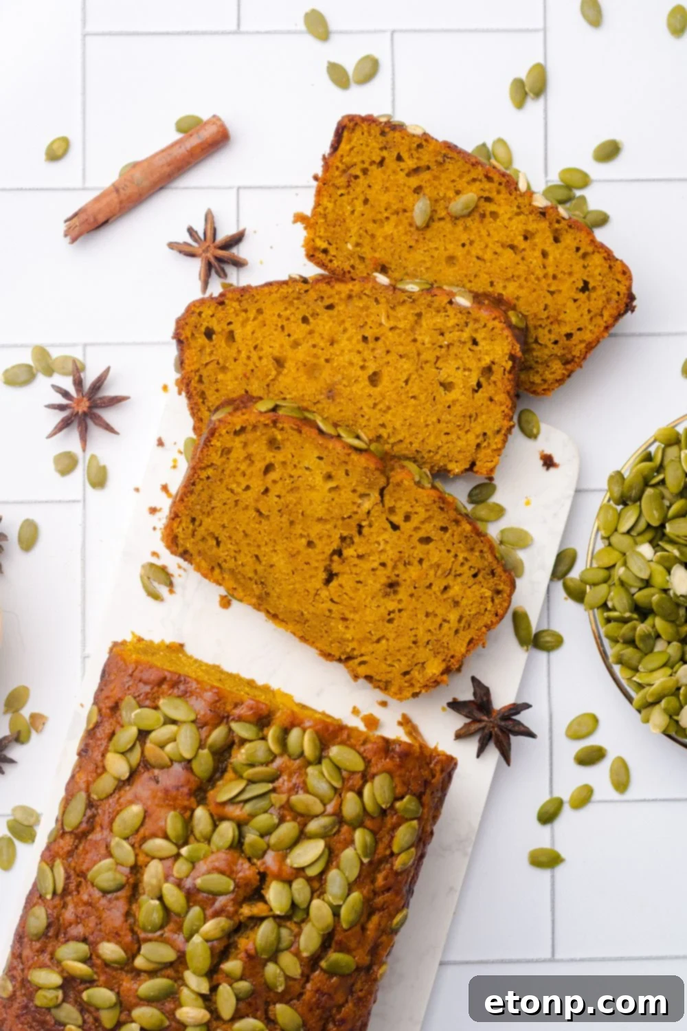 looking down on table to a loaf of Starbucks Pumpkin Bread with three slices placed on table with pumpkin seeds, and cinnamon sticks around the table 