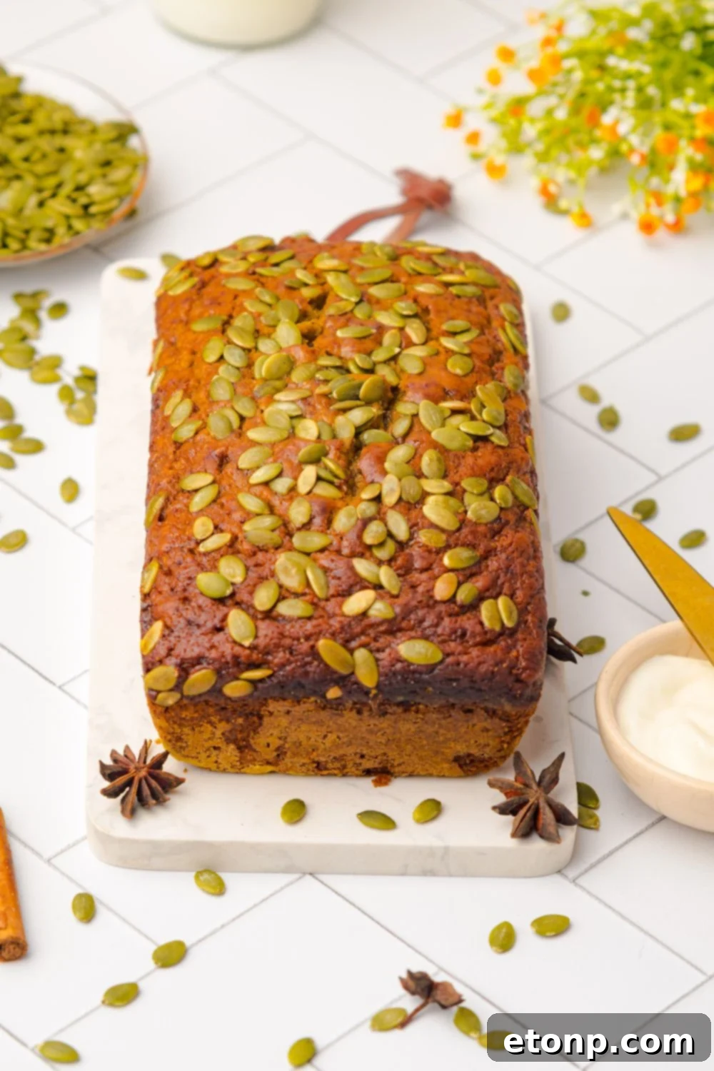 whole loaf of Starbucks Pumpkin Bread on a cutting board on table with seeds and cinnamon sticks scattered around table 