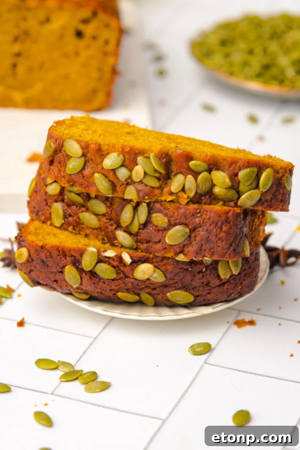 Starbucks Pumpkin Bread stacked on a plate with pumpkin seeds on top of bread and in a bowl to the side 