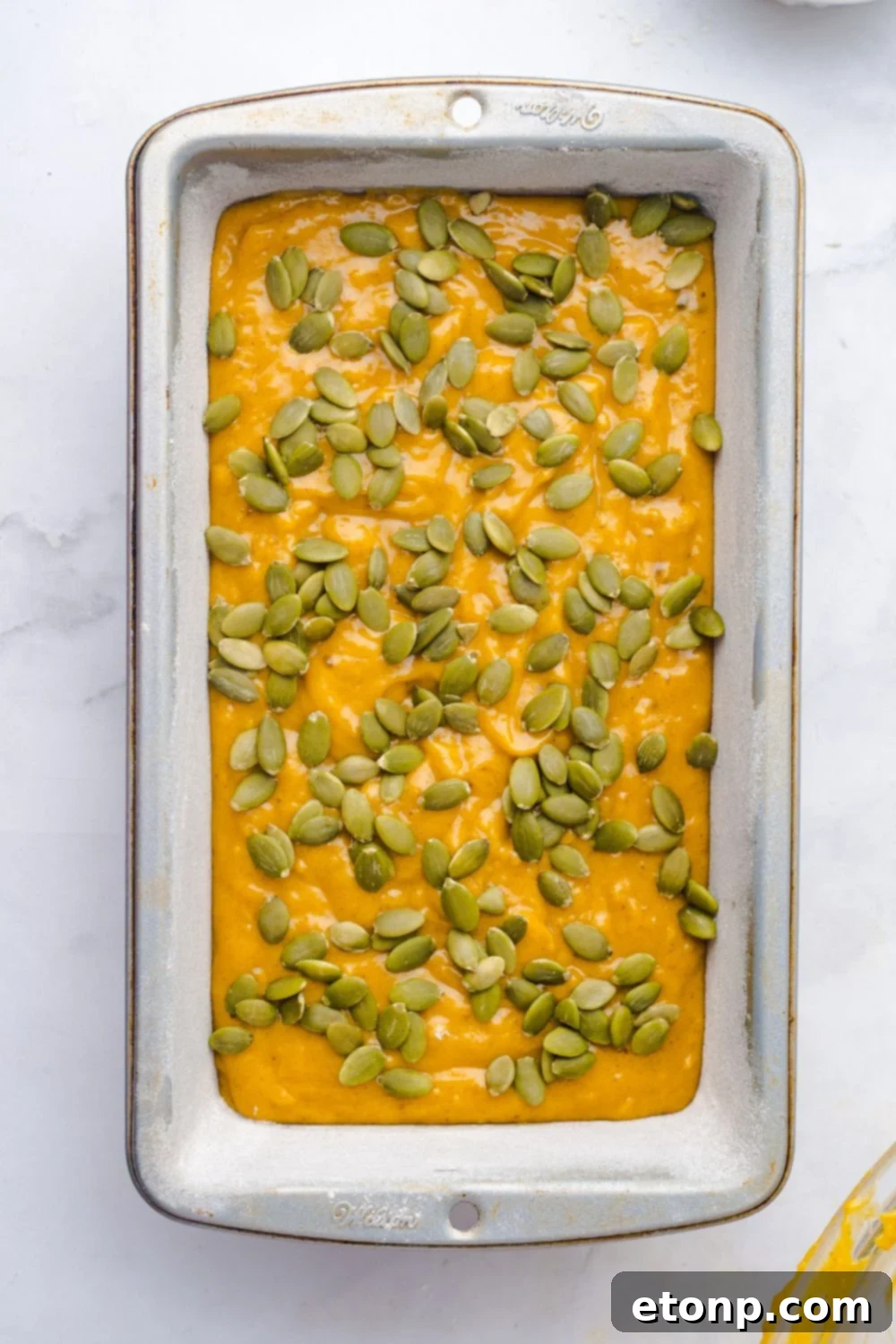 Starbucks Pumpkin Bread batter in a loaf pan on table topped with pumpkin seeds 
