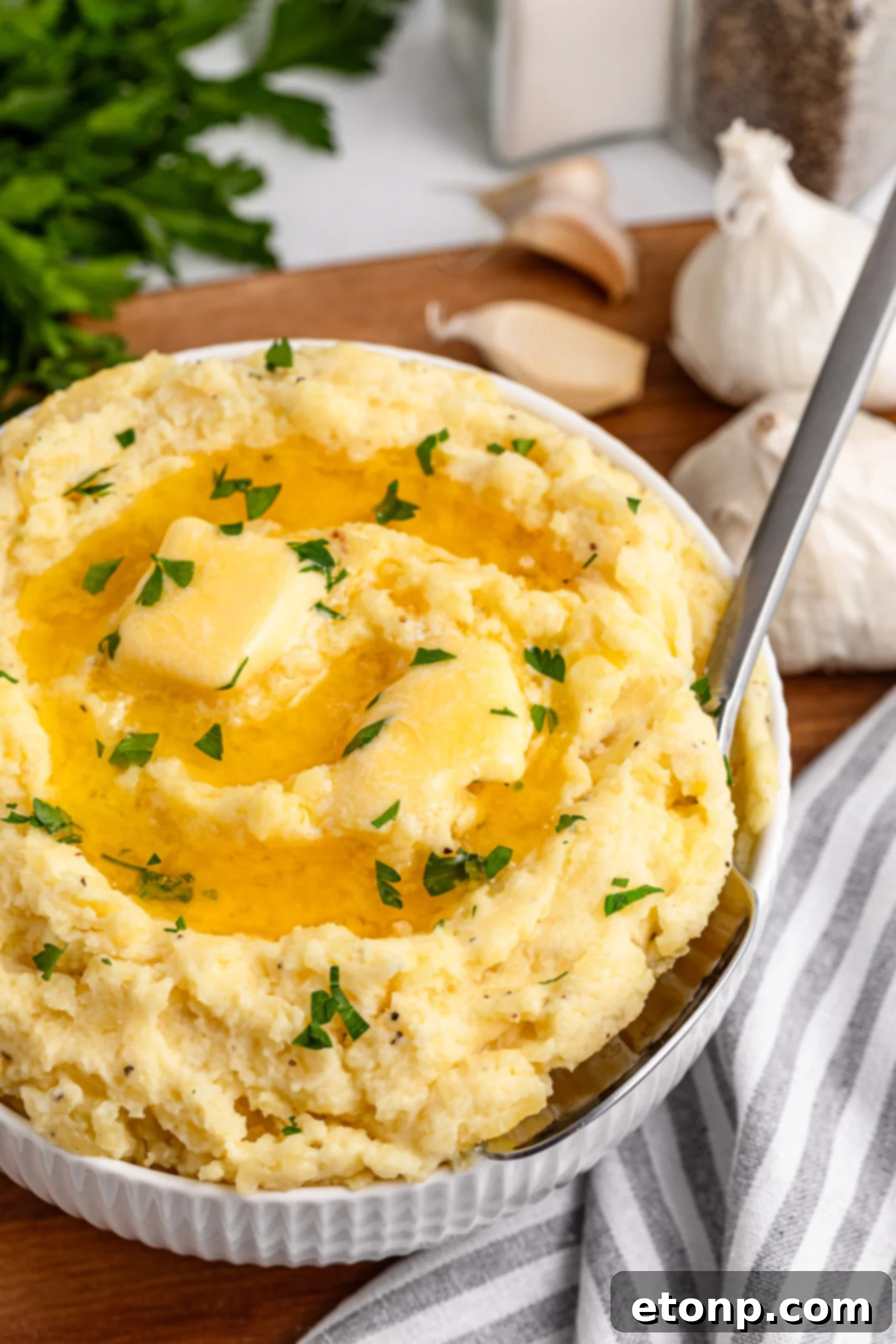 Garlic mashed potatoes in a white bowl on a dark wood table with steam rising