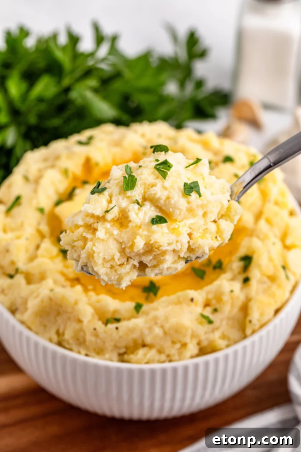 Creamy Garlic Mashed Potatoes with a spoon scooping up some out of the white bowl sitting on a wooden cutting board on the table