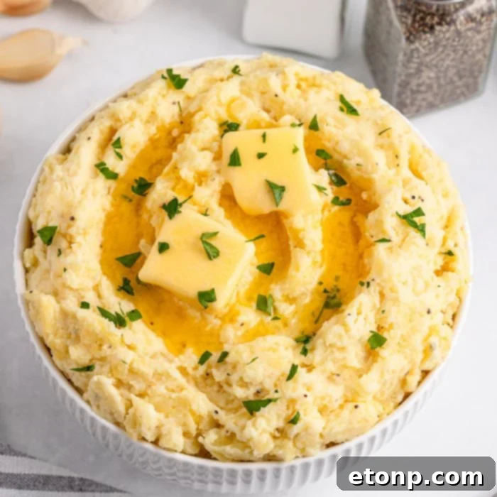 Garlic Mashed Potatoes in a white bowl sitting on a white table with salt and pepper shakers to the side
