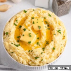 Garlic Mashed Potatoes in a white bowl sitting on a white table with salt and pepper shakers to the side of table