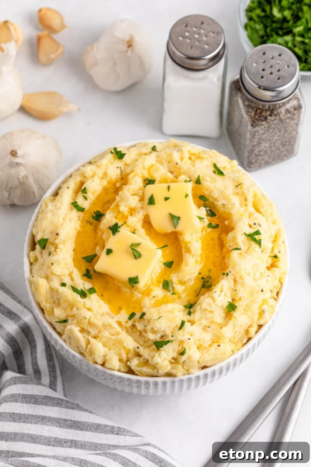 Garlic Mashed Potatoes in a white bowl with slabs of butter melting on top and fresh parsley garnish