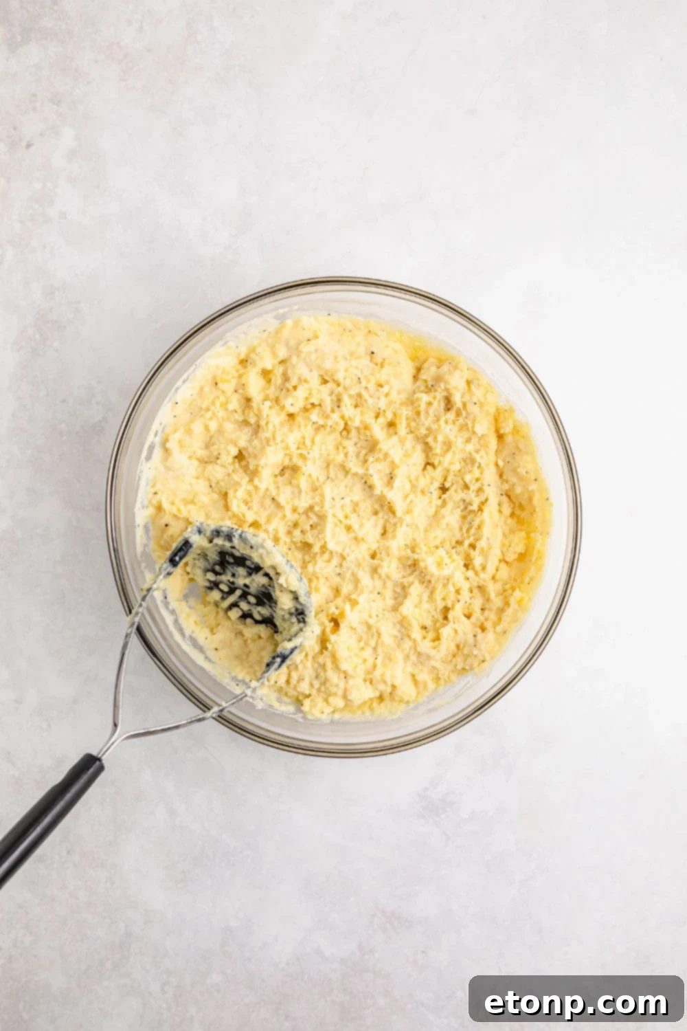 Mashed potatoes in a glass bowl with a potato masher, showing the mashing process