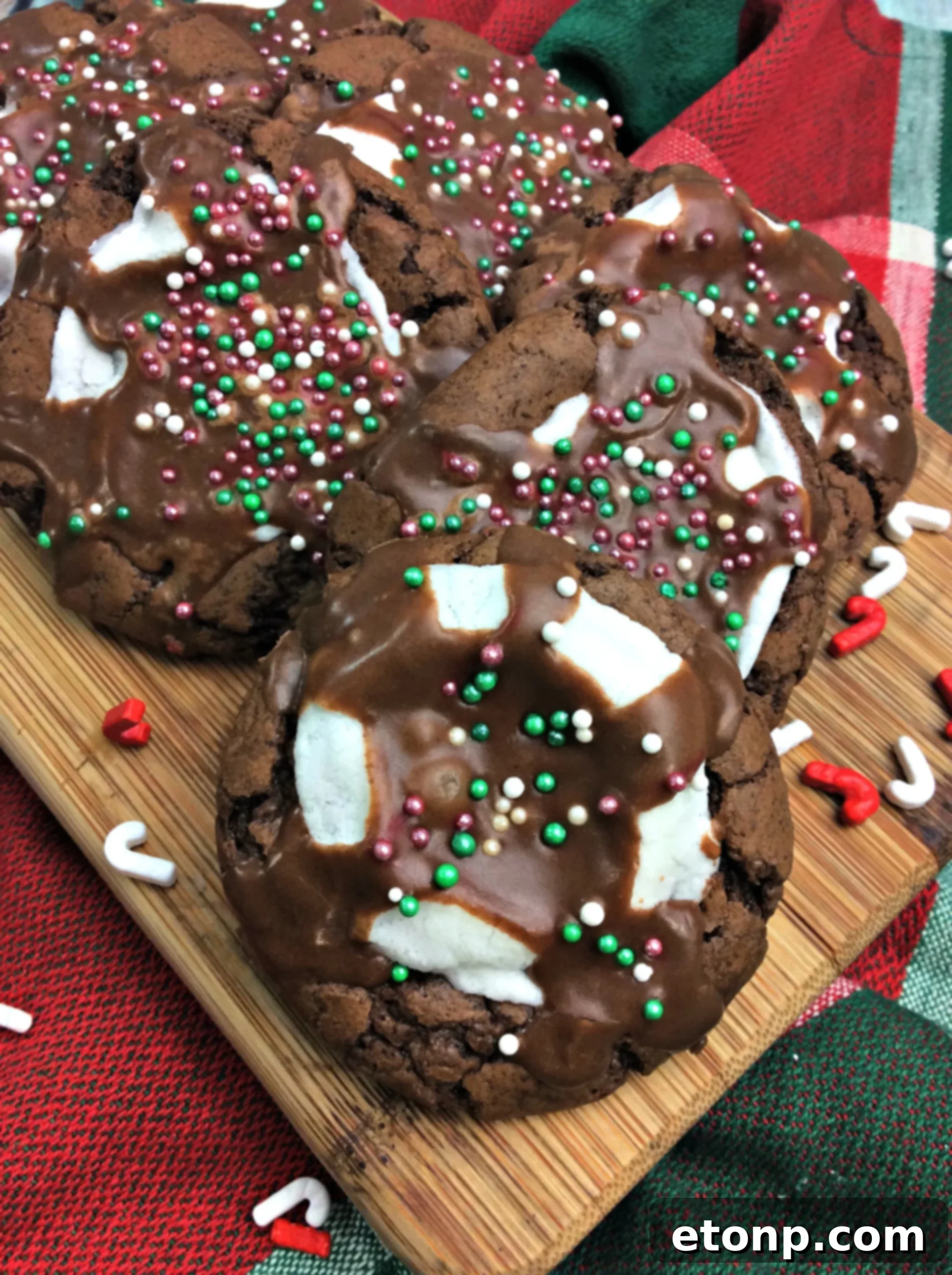 A close-up of a stack of hot cocoa marshmallow cookies, generously topped with chocolate icing and colorful sprinkles, highlighting their irresistible texture.