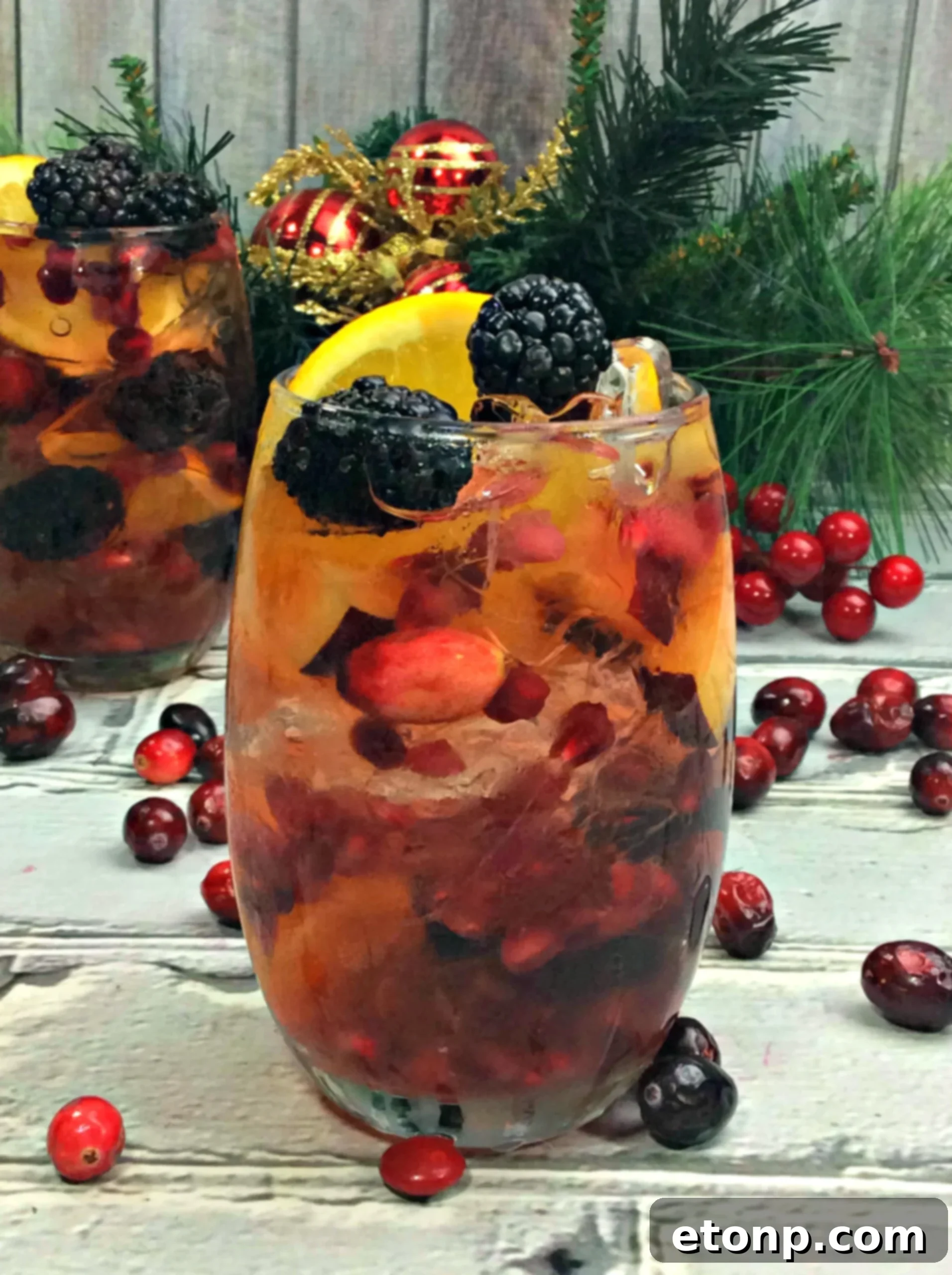 An overhead view of a large pitcher and several glasses of white wine sangria, abundantly filled with fresh fruits like blackberries, cranberries, pomegranate, and orange slices, ready for a party.