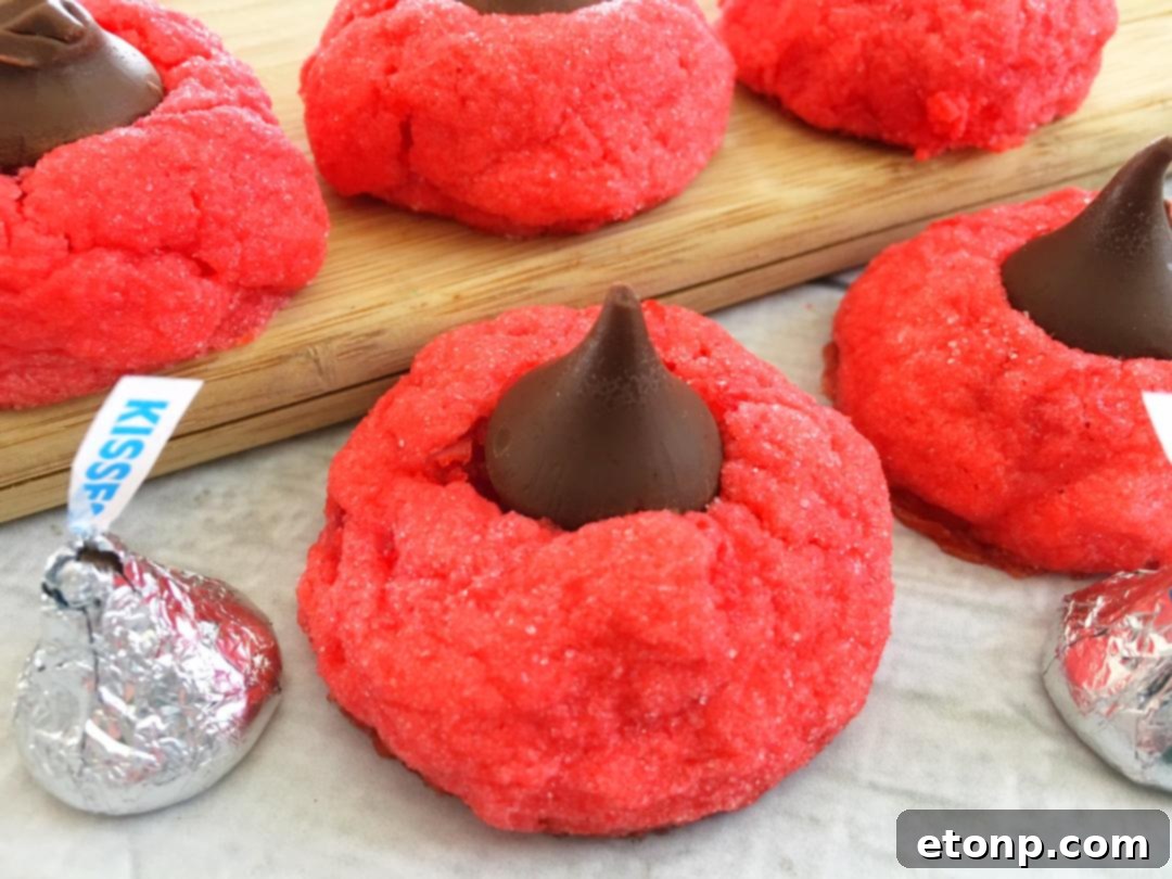 Close-up of freshly baked Cherry Kiss Cookies with a bright red color and a Hershey's Kiss pressed into the center.