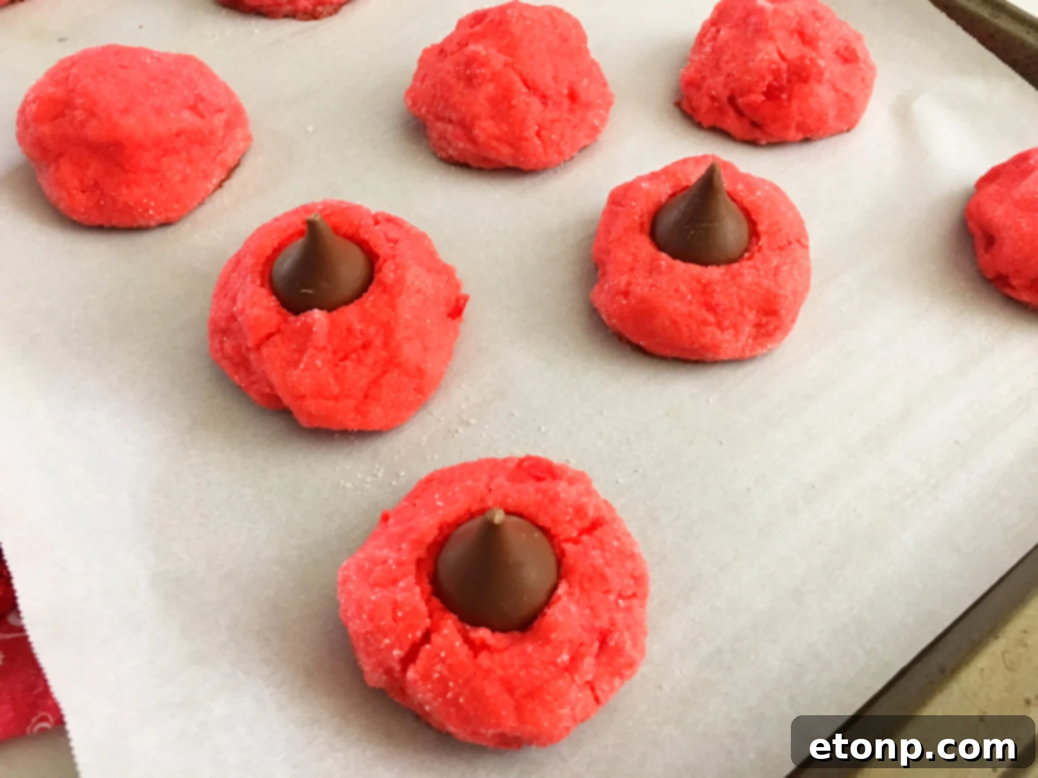 Several Cherry Kiss Cookies arranged on a baking sheet, freshly out of the oven, with some still warm enough for the kisses to settle.