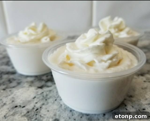 Close-up of a single eggnog jello shot, garnished with whipped cream and a dusting of cinnamon, emphasizing its creamy texture and festive appeal