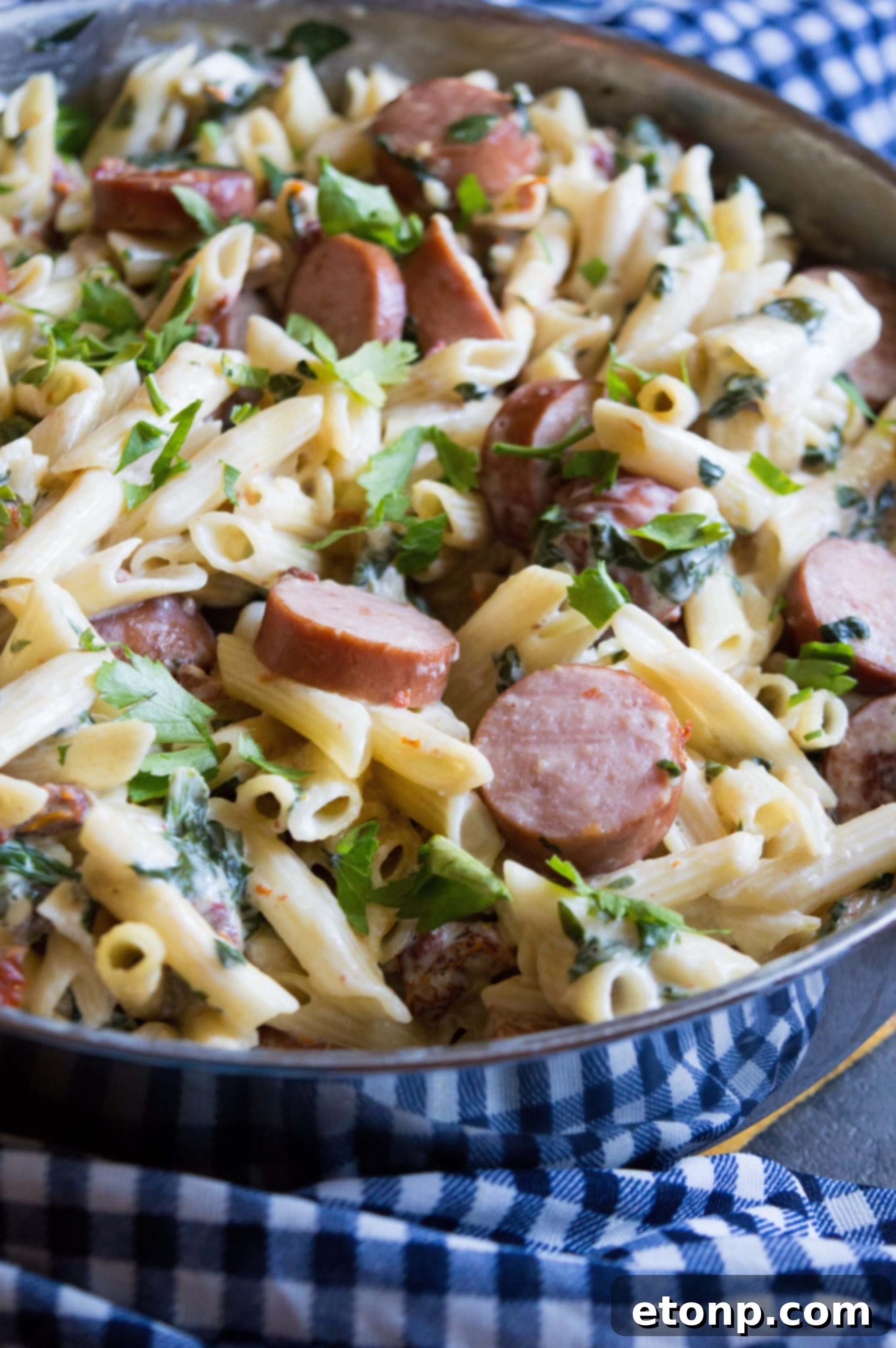 A close-up of a skillet filled with creamy pasta, sliced sausage, and vibrant green spinach.