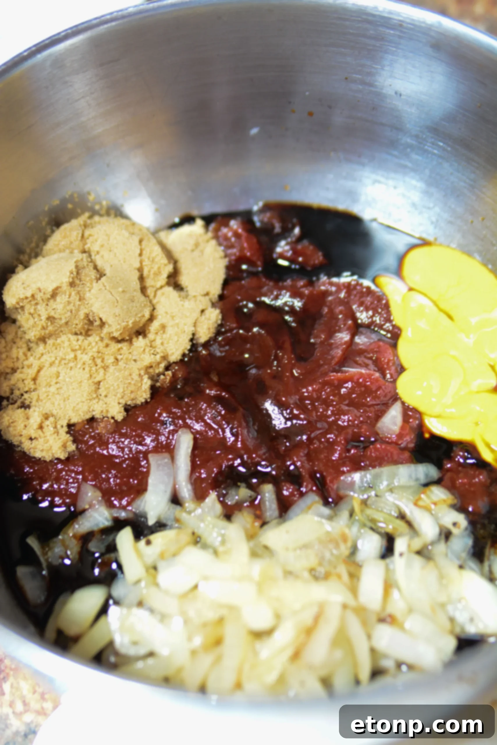 Ultimate Brown Sugar Bacon Baked Beans 3 Close-up of ingredients for brown sugar bacon baked beans including canned beans, onion, molasses, and sauces