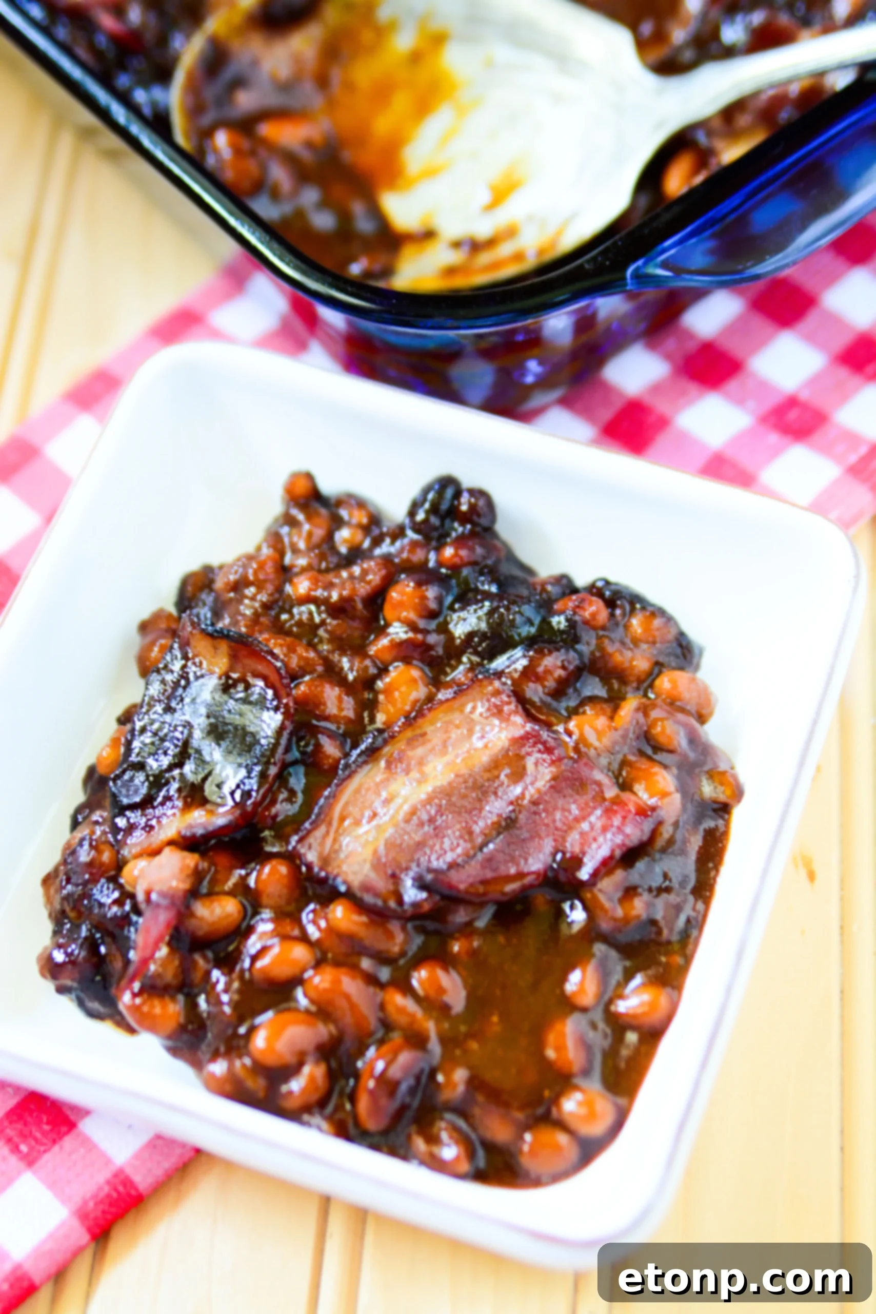 Ultimate Brown Sugar Bacon Baked Beans 7 Serving spoon digging into a dish of brown sugar bacon baked beans