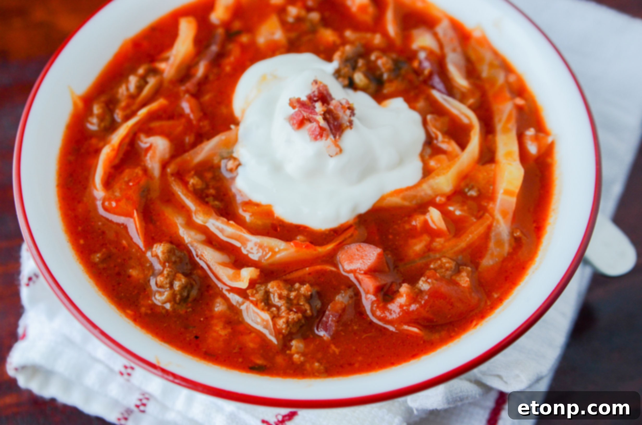 A close-up shot of a steaming bowl of Crockpot Cabbage Roll Soup, garnished with a dollop of sour cream and fresh parsley, on a rustic wooden table.