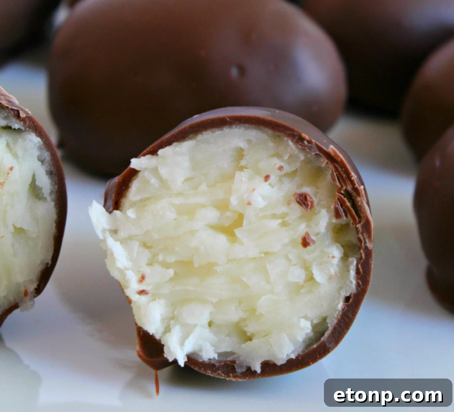 A close-up of a partially dipped coconut cream egg, showing the creamy white coconut filling and the rich chocolate coating.