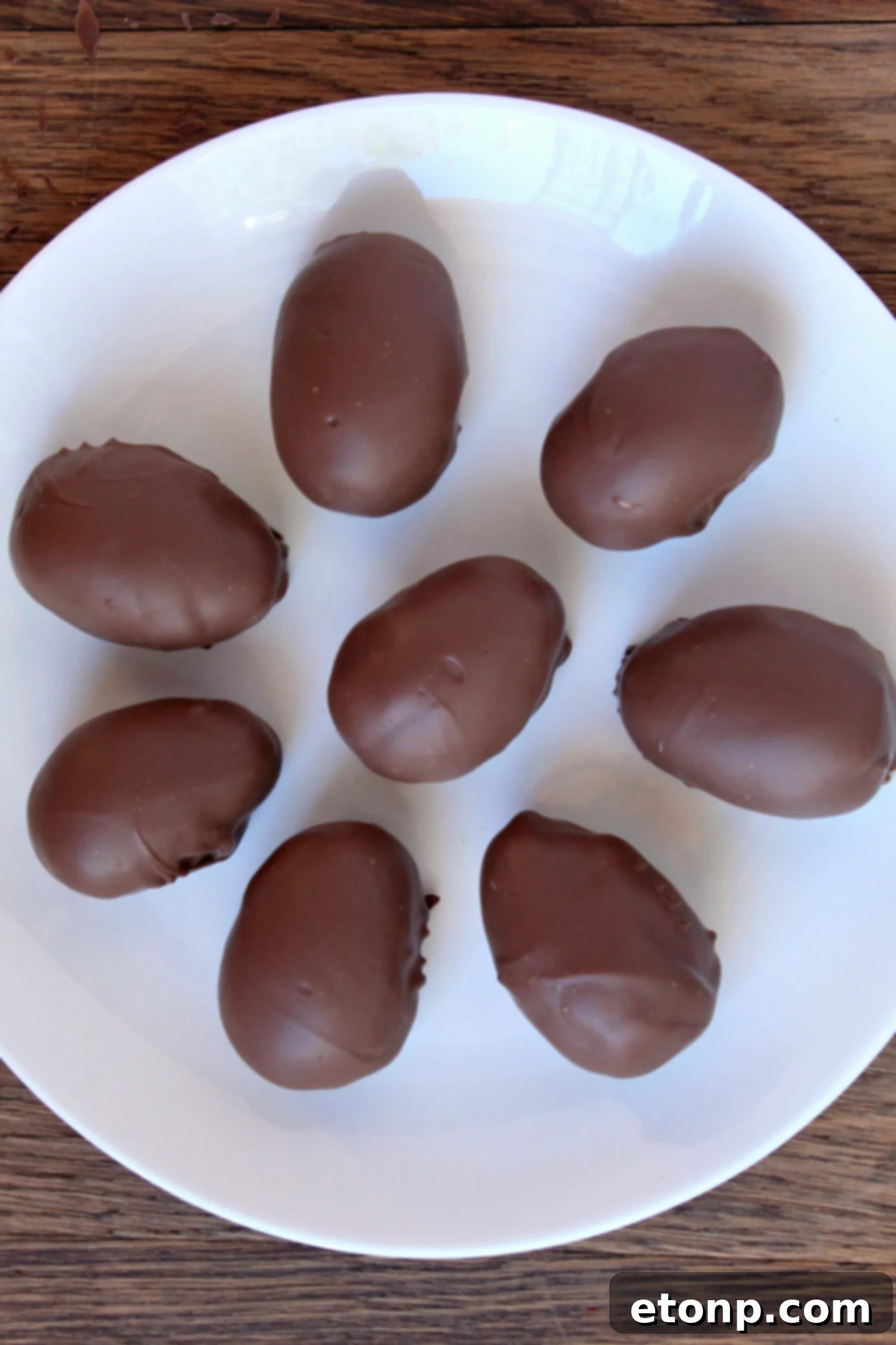 Several perfectly formed chocolate-covered coconut cream eggs arranged neatly on parchment paper, showcasing their delicate coating and texture.