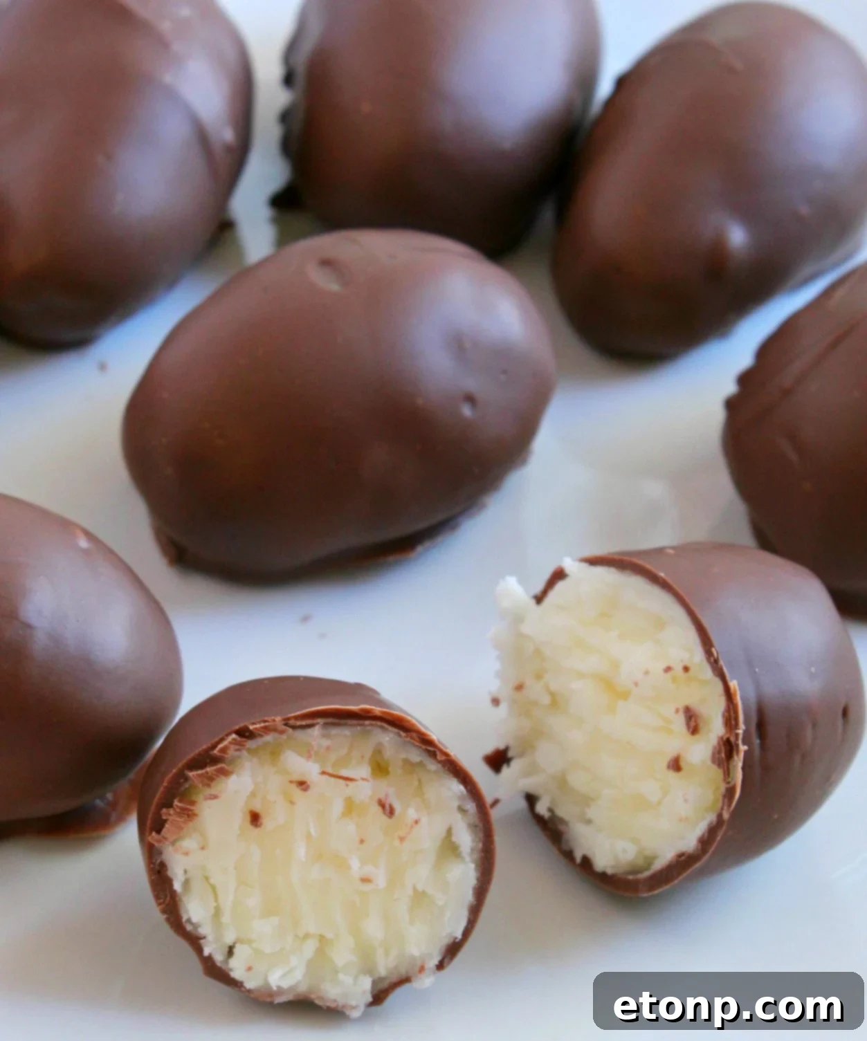 A close-up shot of a single homemade chocolate coconut cream egg with a perfect bite taken out, revealing the moist and fluffy coconut filling inside.