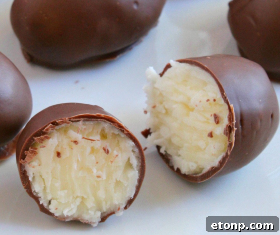 An elegant presentation of several homemade chocolate coconut cream eggs on a white plate, garnished with mint leaves, ready for serving.