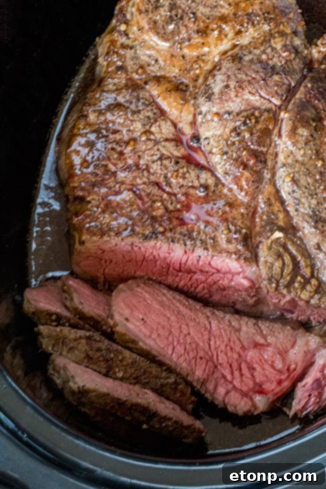 Perfectly cooked and sliced Slow Cooker Roast Beef on a wooden cutting board