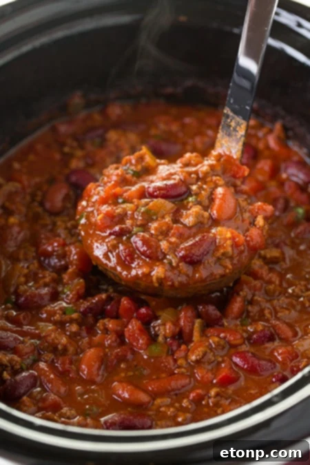 A steaming bowl of classic Slow Cooker Chili, topped with shredded cheese and a dollop of sour cream