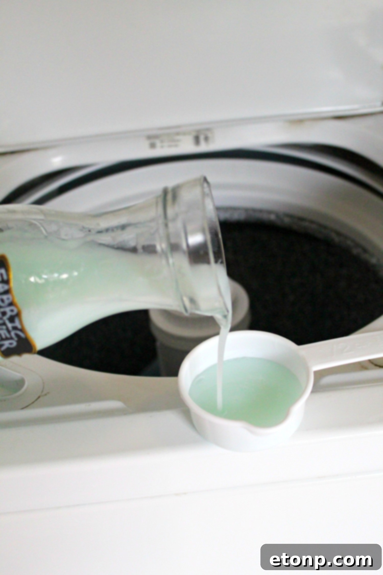 Pouring homemade fabric softener into a washing machine dispenser.