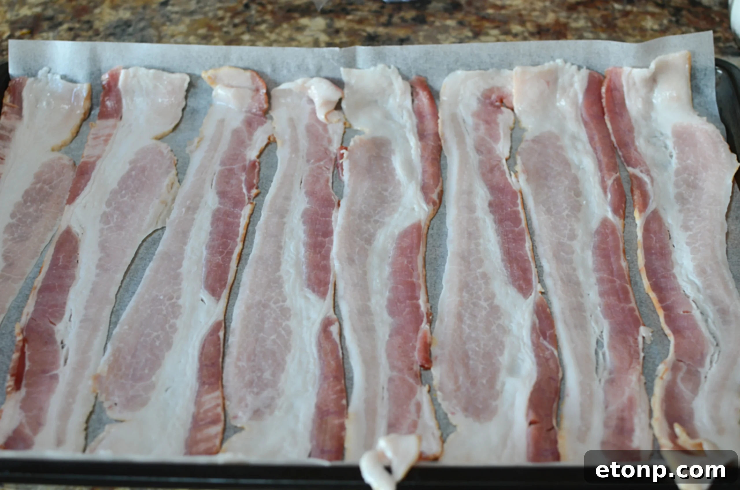 Close-up view of raw bacon strips perfectly spaced on a baking sheet for even cooking