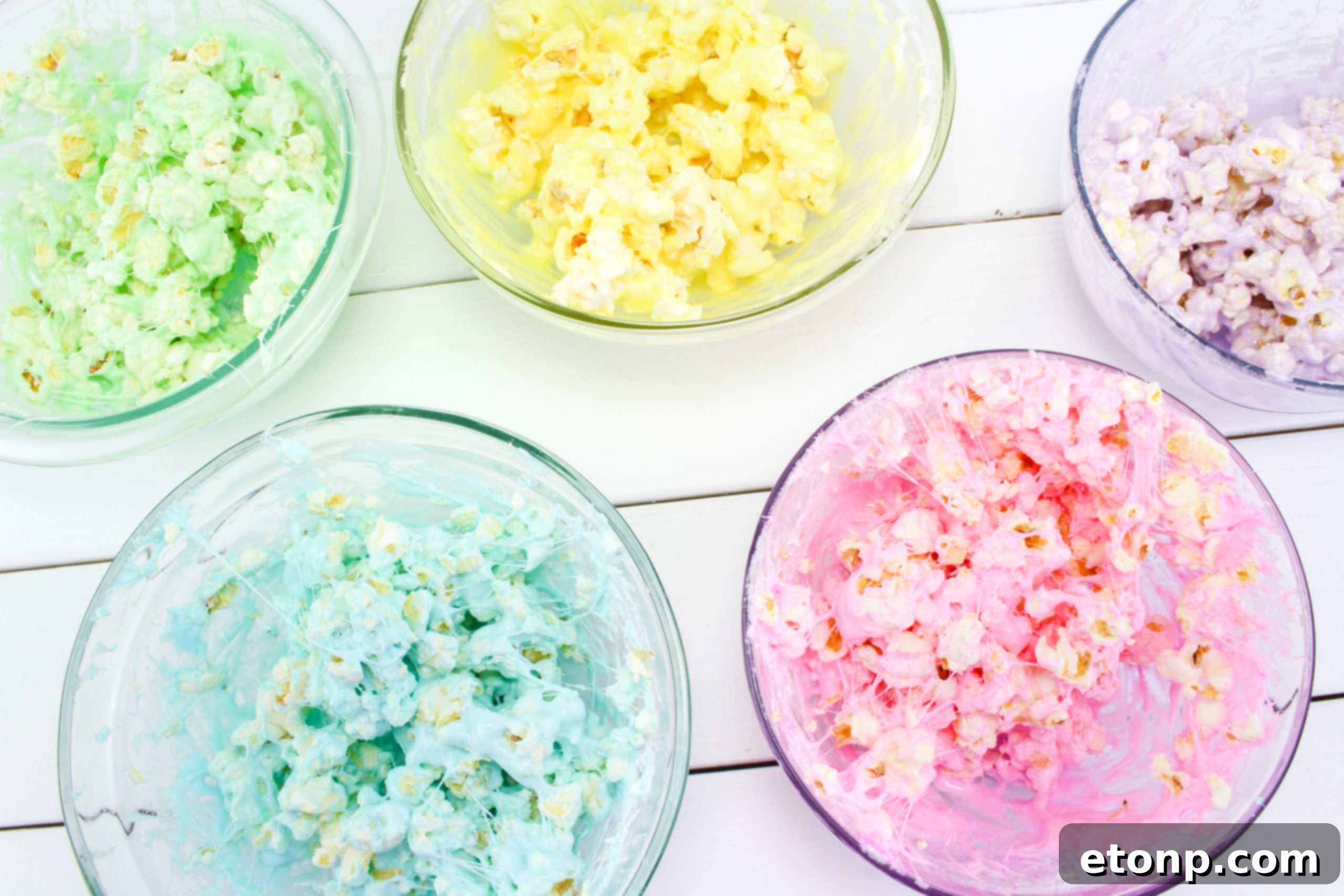 Hand mixing melted PEEPS marshmallow with popped popcorn in a bowl, showing the vibrant colors blending.
