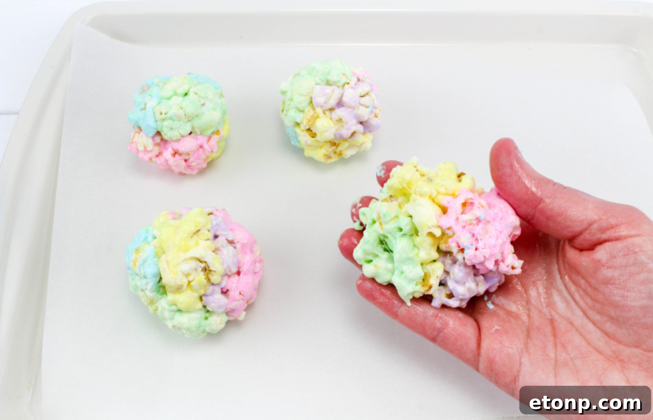Three finished marshmallow popcorn balls, showcasing a swirl of multiple spring colors, ready to be enjoyed.
