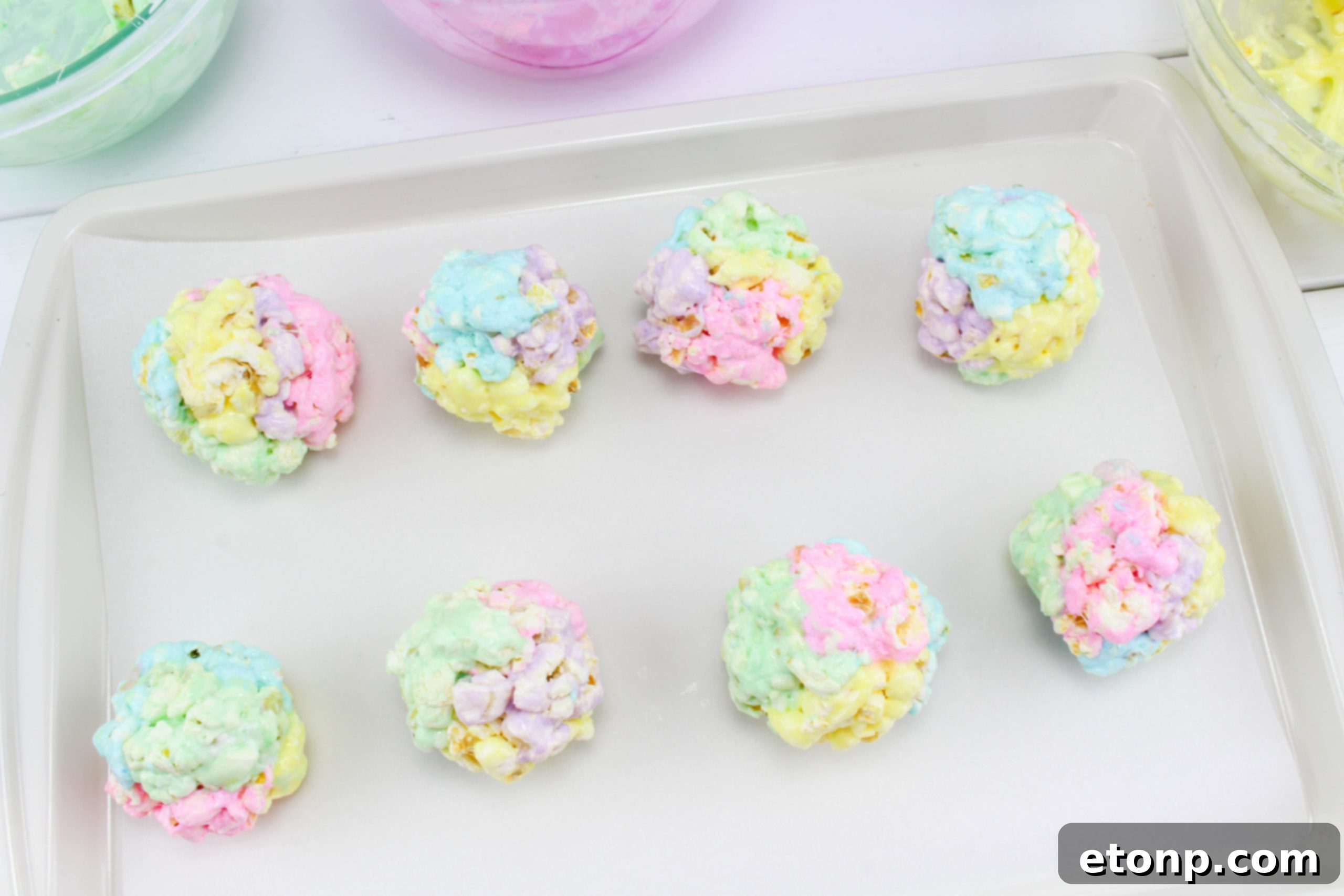 Overhead view of several multi-colored marshmallow popcorn balls arranged on a serving plate.
