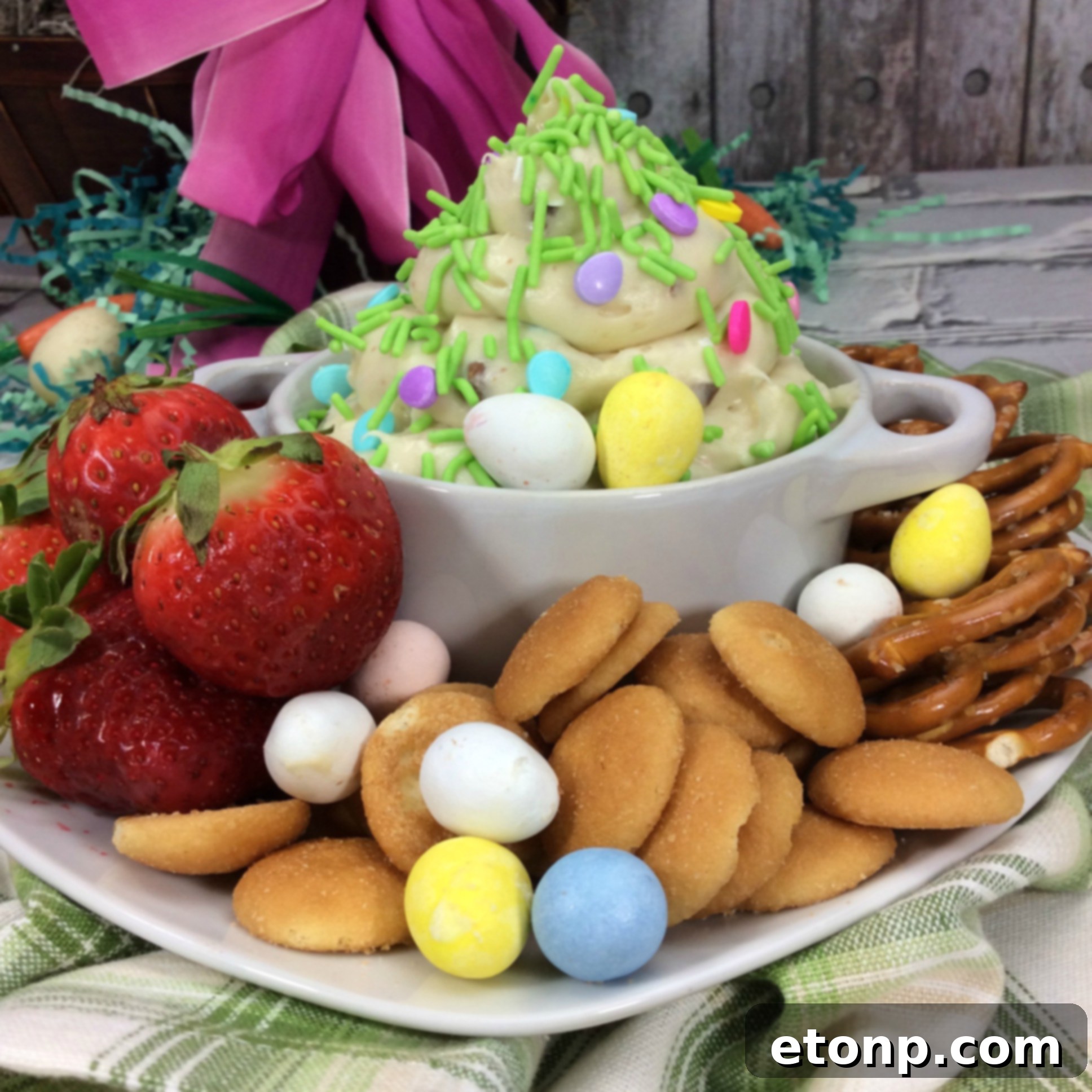 Overhead shot of Springtime Cheesecake Dip in a white bowl, garnished with whole Cadbury Mini Eggs, and surrounded by various dippers including graham crackers, vanilla wafers, and fresh fruit.